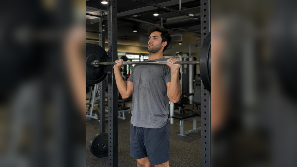 man performing an overhead press with a barbell in a gym