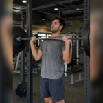 man performing an overhead press with a barbell in a gym